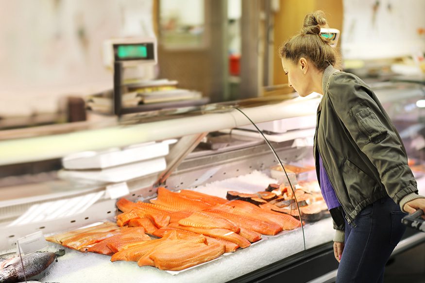 woman looking at salmon steaks in a grocery case
